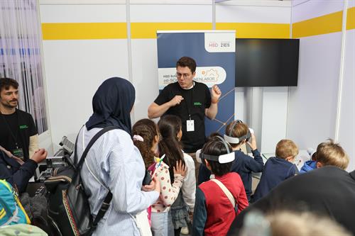 Kinder testen bei einer Hochschulveranstaltung gemeinsam mit einem Mitarbeiter Virtual-Reality-Brillen.
