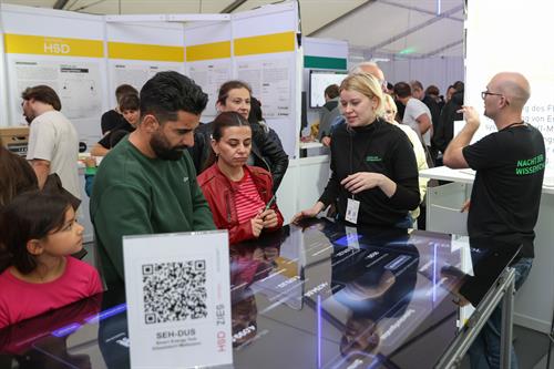 Besucherinnen und Besucher informieren sich an einem Hochschulstand über digitale Lösungen für die energetische Gebäudesanierung.