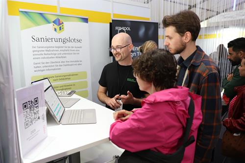 Ein Hochschulmitarbeiter erklärt Besucherinnen und Besuchern eine digitale Anwendung zur energetischen Gebäudesanierung.