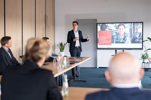 Person hält eine Präsentation zu einem Studien- und Weiterbildungsangebot im Bereich Haus-, Energie- und Anlagentechnik (HEAT) vor einer kleinen Gruppe in einem Konferenzraum.